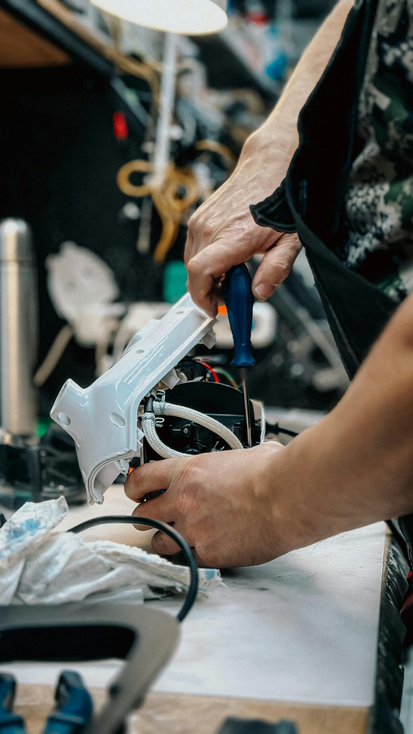 Technician using screwdriver to fix an electronic device at a workbench.